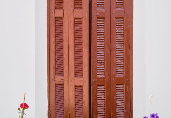 Wooden shutters and flower pots in front of an old traditional house in the city of Lindos on the island of Rhodes, the Greek islands of the Dodecanese archipelago, a popular tourism destination